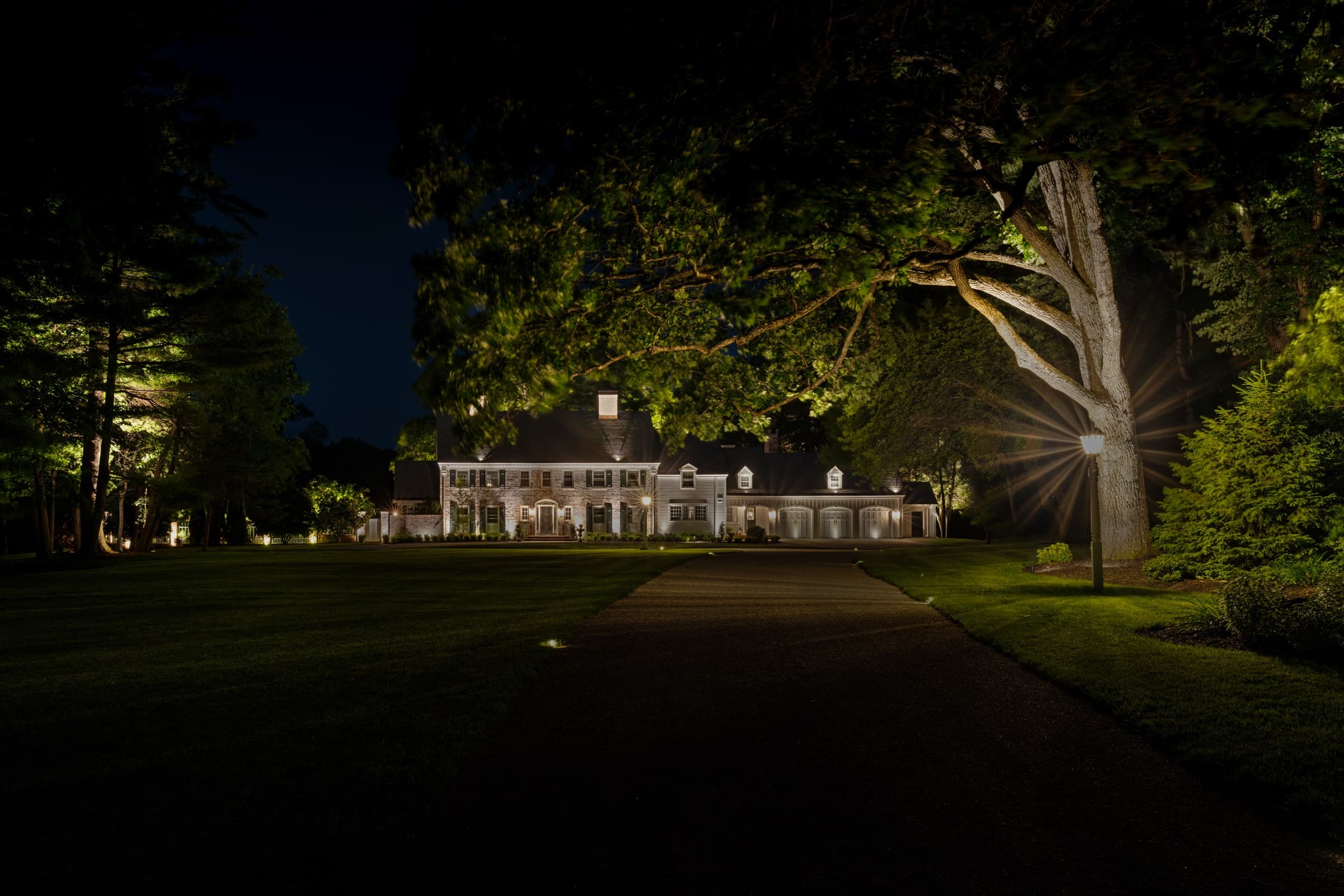 The house at the end of a long drive, a mature tree uplit from its base